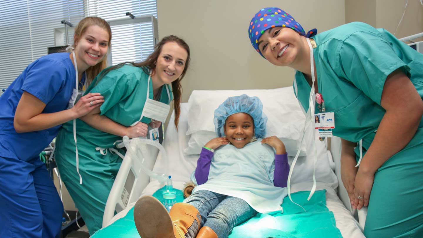 Three nurses around bed with young child as a patient